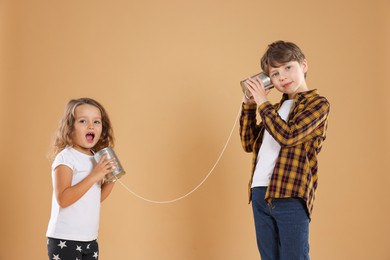 Photo of Boy and girl talking on tin can telephone against beige background