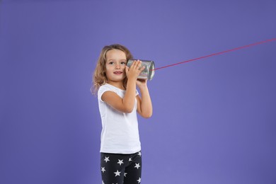 Girl using tin can telephone on violet background