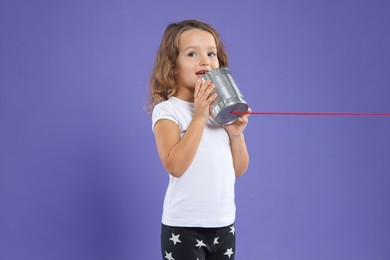 Girl using tin can telephone on violet background