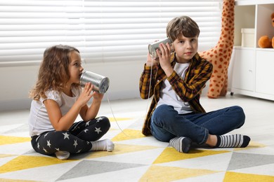 Photo of Boy and girl talking on tin can telephone indoors