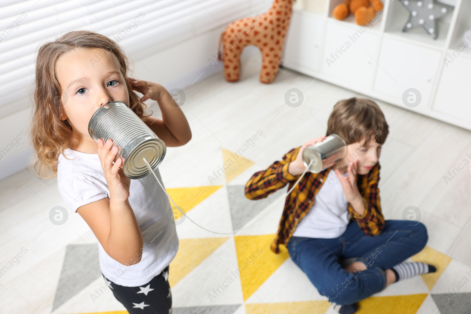 Photo of Boy and girl talking on tin can telephone indoors, above view