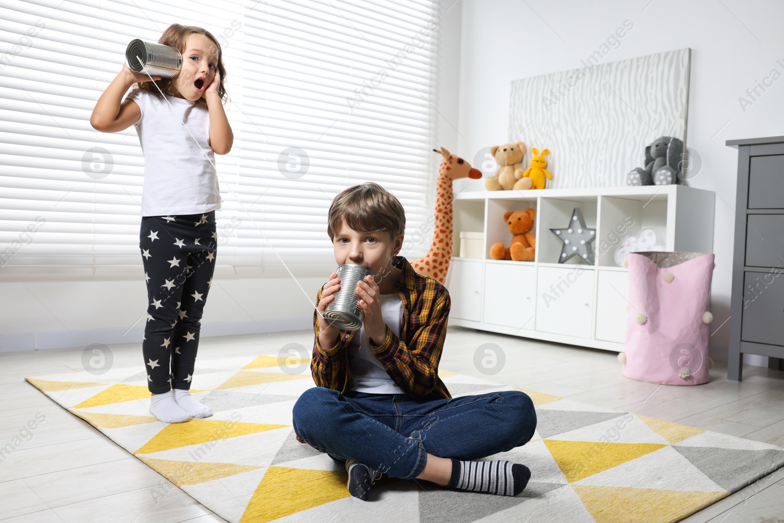 Photo of Boy and girl talking on tin can telephone indoors