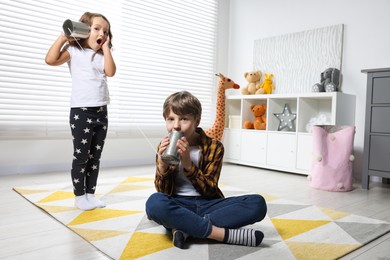 Boy and girl talking on tin can telephone indoors