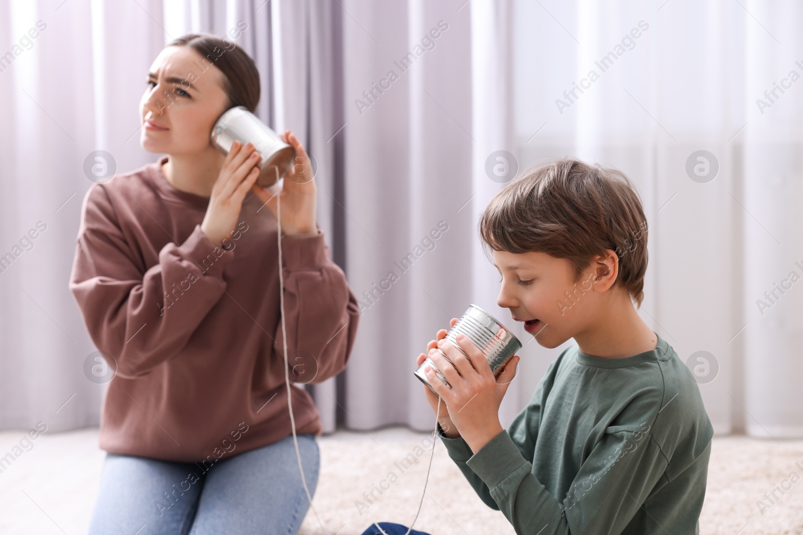 Photo of Woman and boy talking on tin can telephone indoors