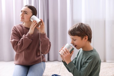 Photo of Woman and boy talking on tin can telephone indoors