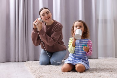 Woman and girl talking on tin can telephone indoors