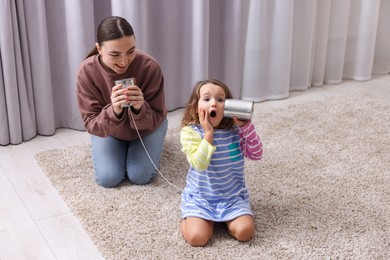 Photo of Woman and girl talking on tin can telephone indoors