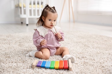 Photo of Cute little girl playing with toy xylophone on floor at home