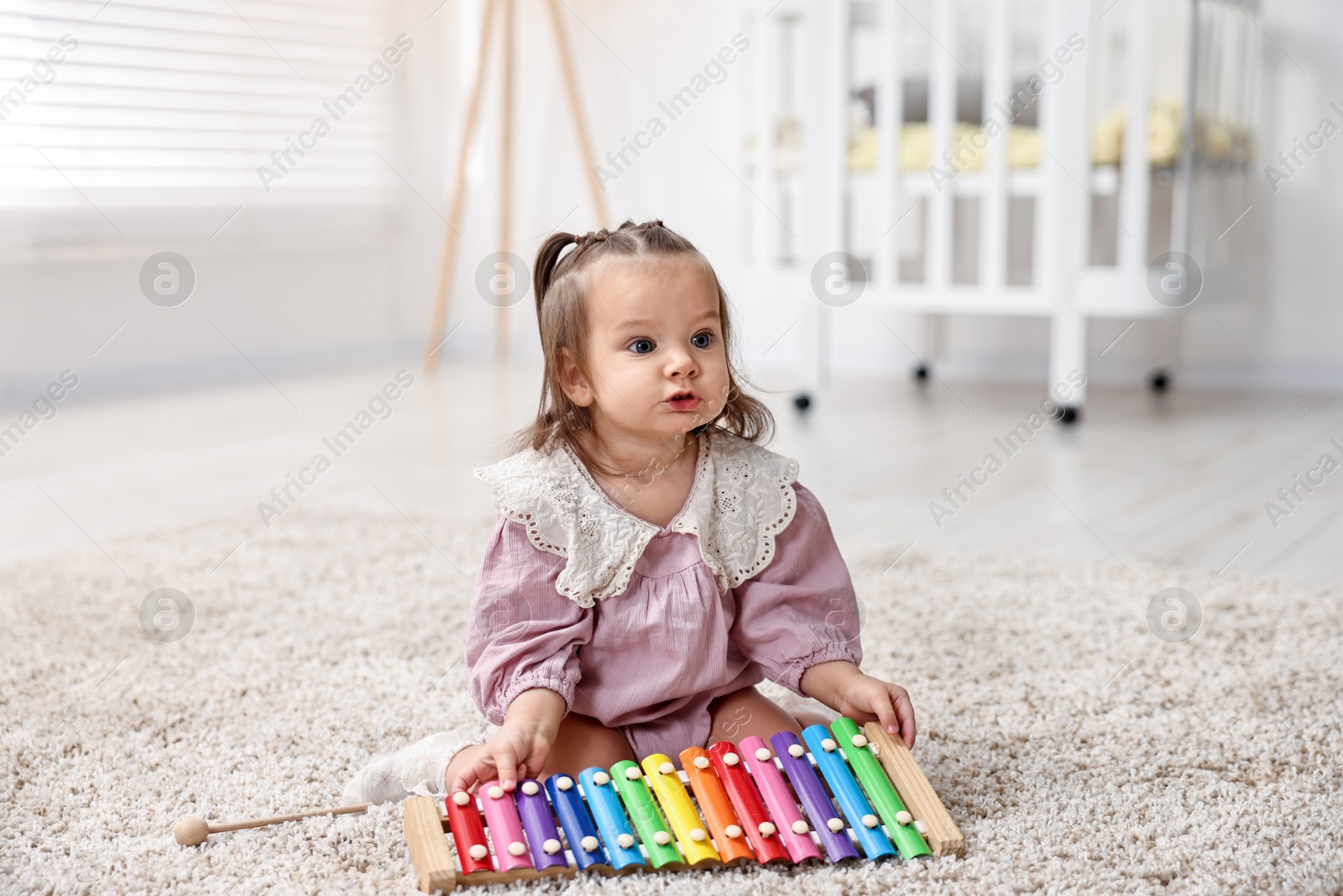 Photo of Cute little girl playing with toy xylophone on floor at home