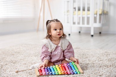 Photo of Cute little girl playing with toy xylophone on floor at home