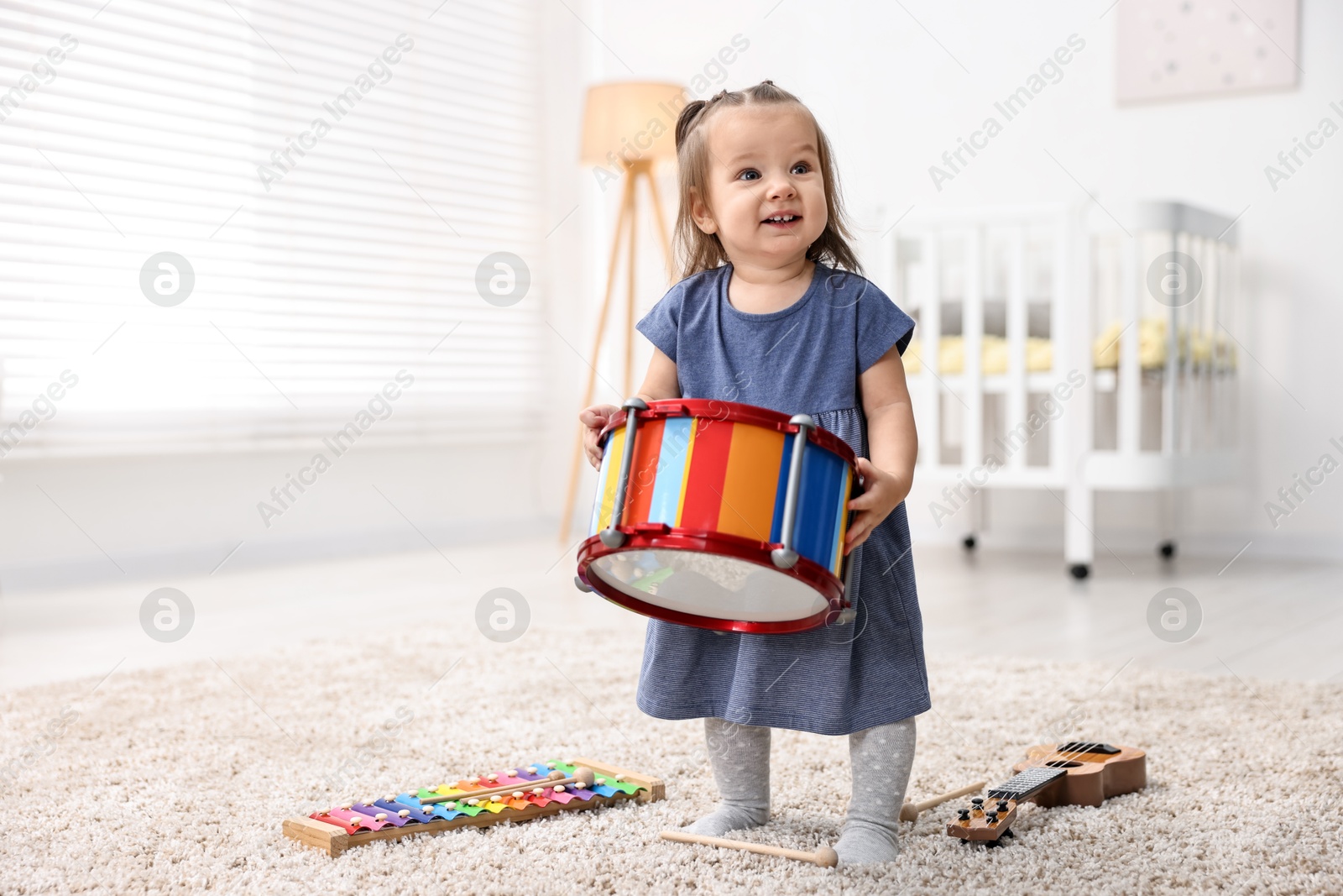 Photo of Cute little girl playing with toy drum on floor at home, space for text