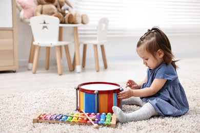 Photo of Cute little girl playing with toy drum on floor at home