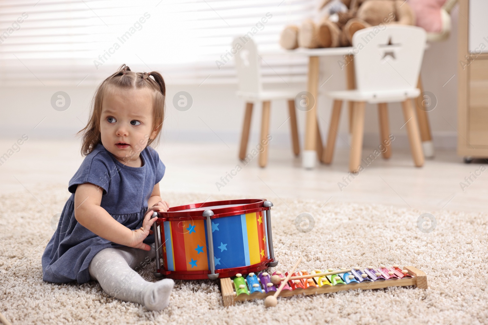 Photo of Cute little girl playing with toy drum on floor at home, space for text