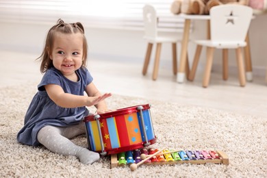 Photo of Cute little girl playing with toy drum on floor at home, space for text