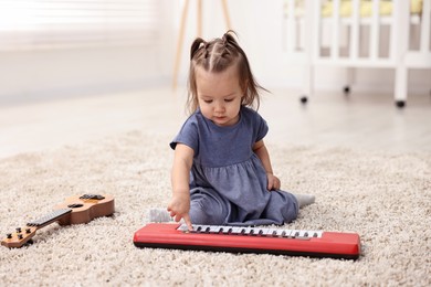 Photo of Cute little girl playing with toy piano at home