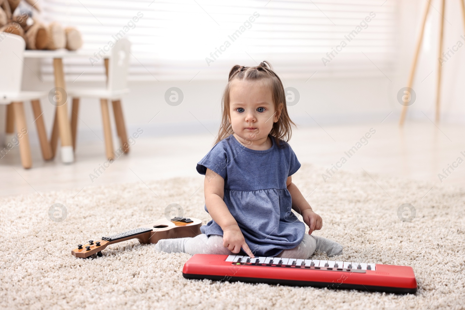 Photo of Cute little girl playing with toy piano at home