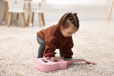 Photo of Cute little girl playing with toy guitar on floor at home