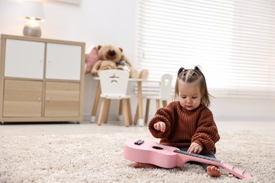 Photo of Cute little girl playing with toy guitar on floor at home, space for text