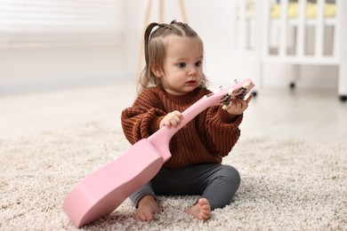 Photo of Cute little girl playing with toy guitar on floor at home