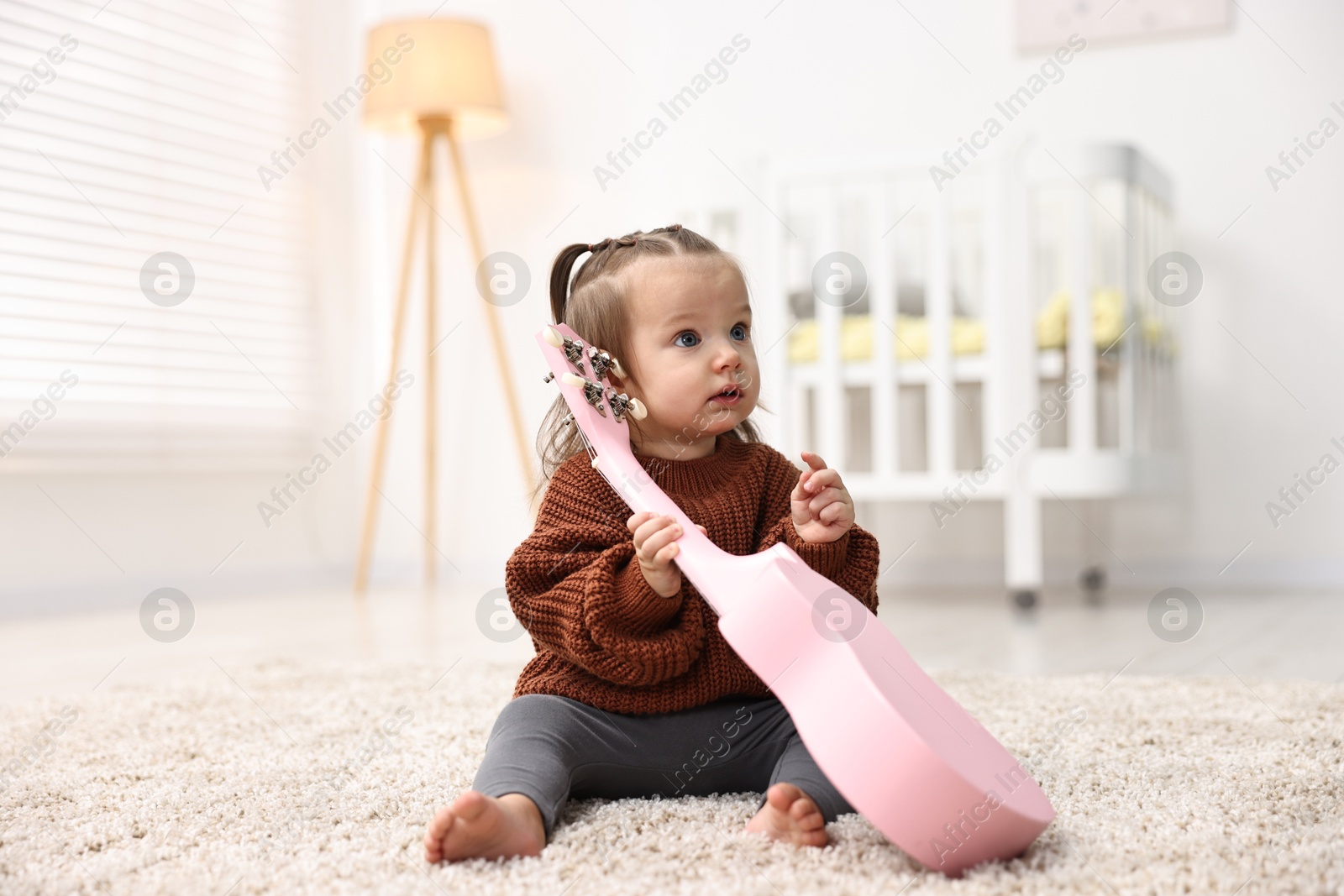 Photo of Cute little girl playing with toy guitar on floor at home