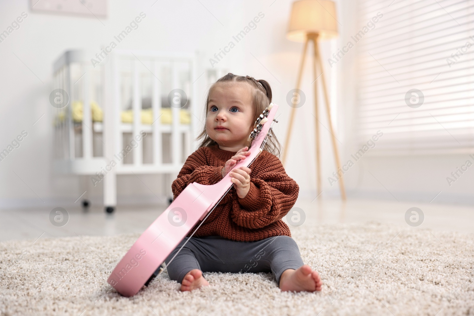 Photo of Cute little girl playing with toy guitar on floor at home