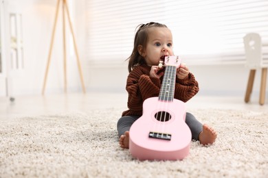 Photo of Cute little girl playing with toy guitar on floor at home, space for text