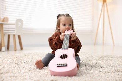 Photo of Cute little girl playing with toy guitar on floor at home