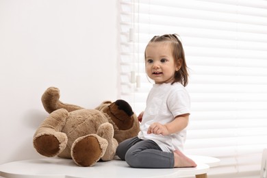 Photo of Cute little girl with teddy bear on table indoors