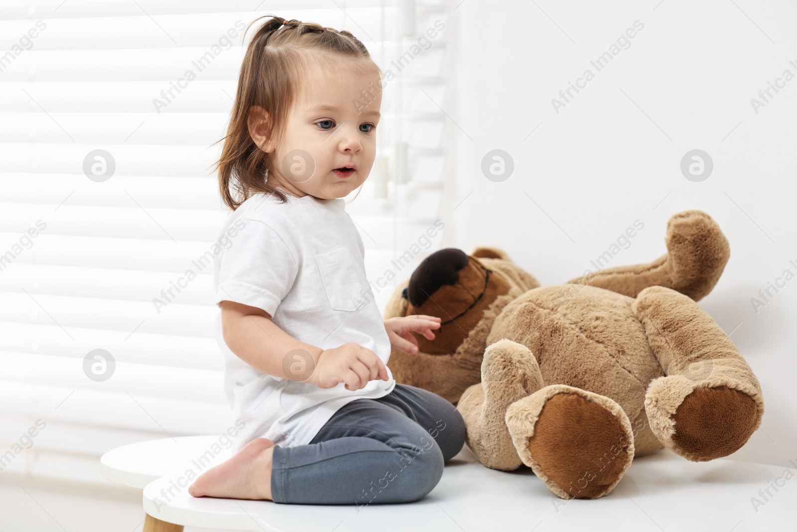 Photo of Cute little girl with teddy bear on table indoors