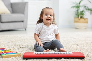 Photo of Cute little girl playing with toy piano at home