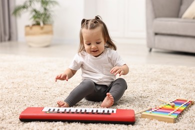 Photo of Cute little girl playing with toy piano at home