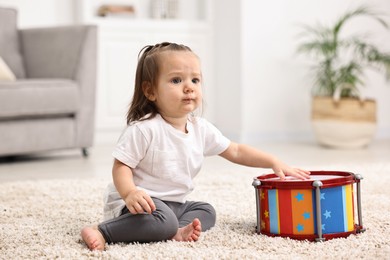 Photo of Cute little girl playing with toy drum on floor at home