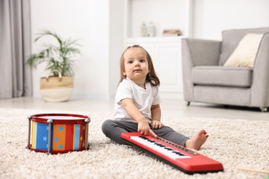 Photo of Cute little girl playing with toy piano at home