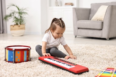 Photo of Cute little girl playing with toy piano at home