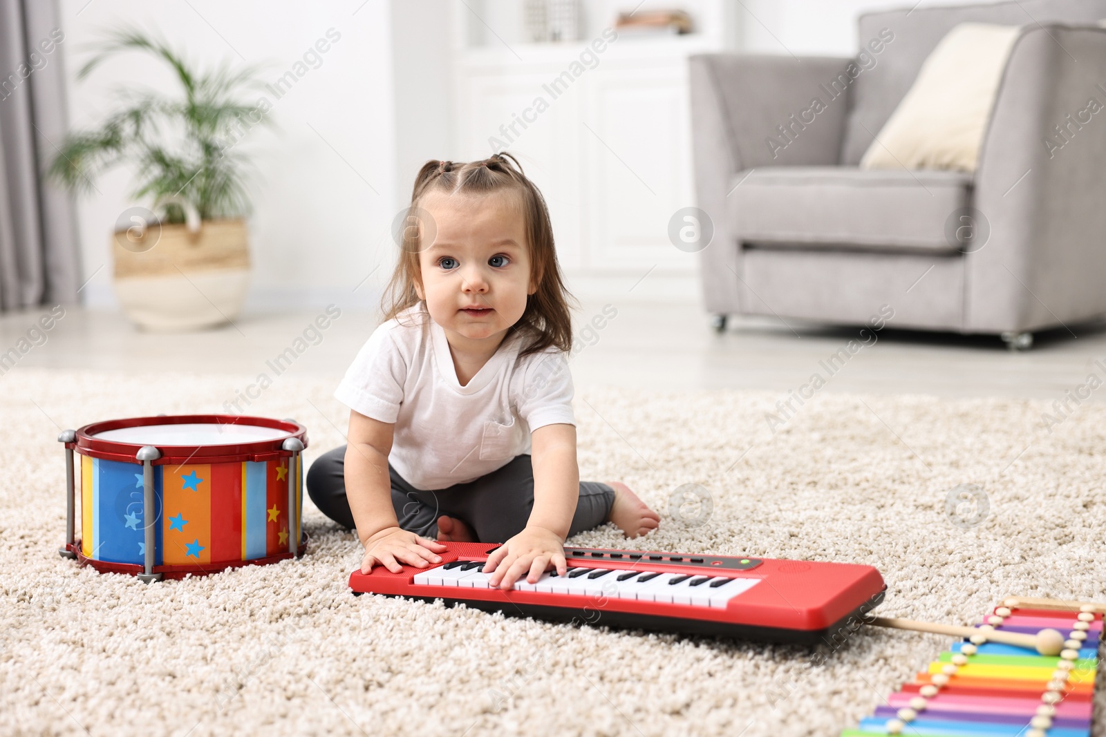 Photo of Cute little girl playing with toy piano at home