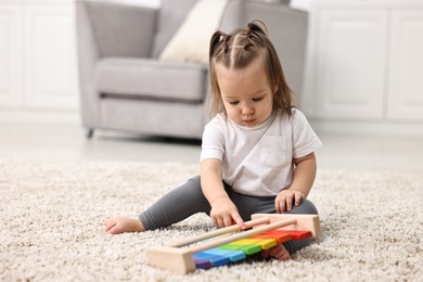 Photo of Cute little girl playing with toy xylophone on floor at home