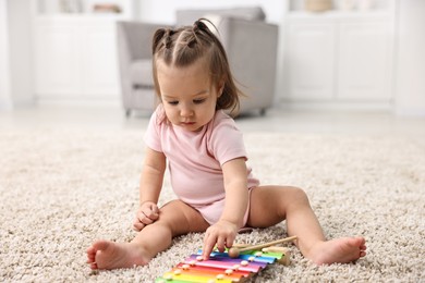 Photo of Cute little girl playing with toy xylophone on floor at home