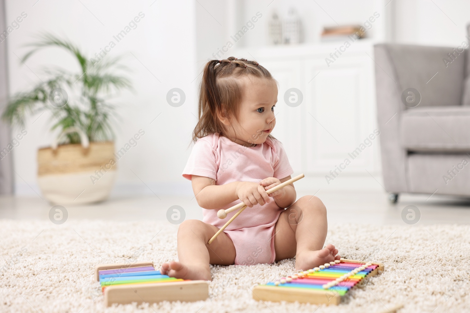 Photo of Cute little girl playing with toy xylophones on floor at home