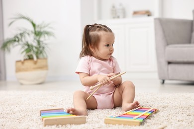 Photo of Cute little girl playing with toy xylophones on floor at home