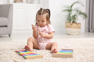 Photo of Cute little girl playing with toy xylophones on floor at home