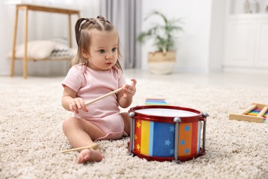 Photo of Cute little girl playing with toy drum and drumsticks on floor at home