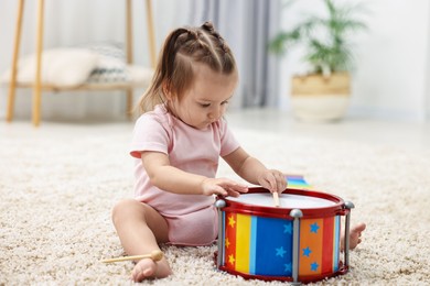 Photo of Cute little girl playing with toy drum and drumsticks on floor at home