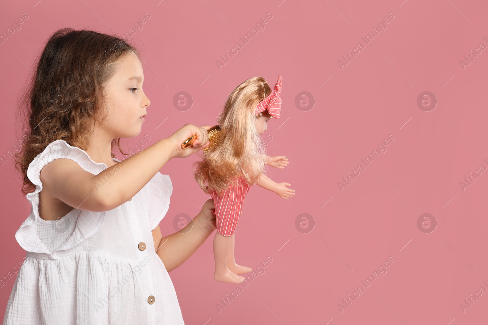 Photo of Cute little girl brushing doll's hair on pink background. Space for text