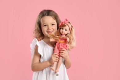 Photo of Cute little girl with doll and brush on pink background