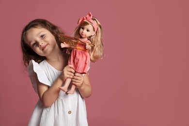 Photo of Cute little girl with doll and brush on pink background. Space for text