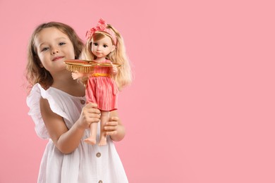 Photo of Cute little girl with doll and brush on pink background. Space for text