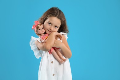 Photo of Cute little girl embracing her doll on light blue background