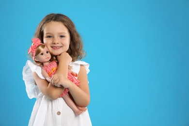 Photo of Cute little girl embracing her doll on light blue background. Space for text