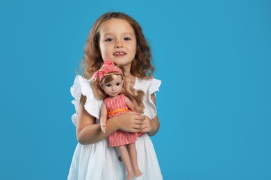 Photo of Cute little girl with doll on light blue background