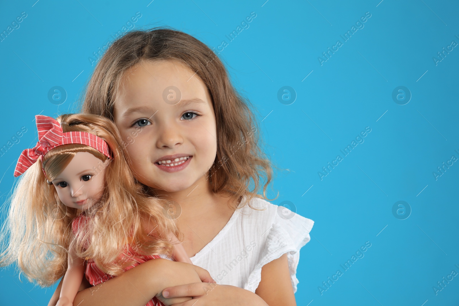 Photo of Cute little girl with doll on light blue background. Space for text